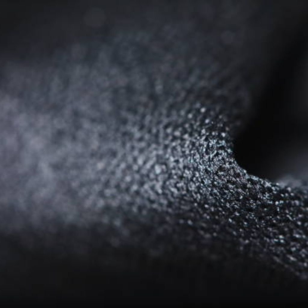 Neo Dry Tech Fabric: Ultimate Moisture Control for Athletes 7 Close-up macro view of a dark textured fabric surface with fine grain and soft lighting, highlighting a curved fold.Neo Dry Tech Fabric: