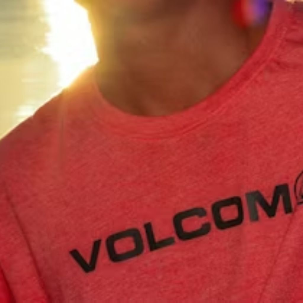 Velocity Dry Tech Knit: High-Performance Fabric for Athletes 7 Red short-sleeve Volcom t-shirt with bold white “VOLCOM” chest print; smooth fabric with soft light reflection; blurred sunny background.
Velocity Dry Tech Knit: