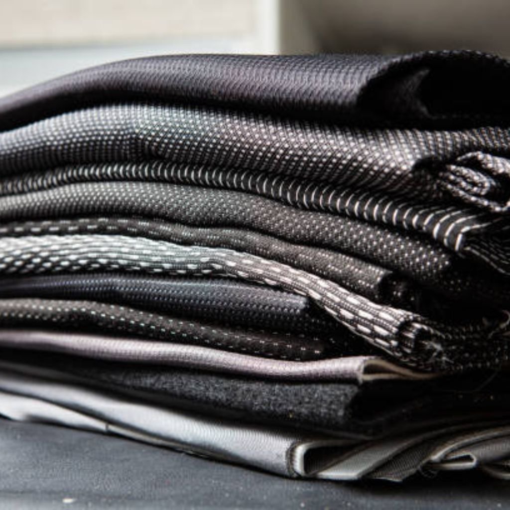Infinity Dry Performance Fabric: Sweat-Wicking Comfort Gear 9 Stack of folded dark-colored textured fabrics with a subtle dotted pattern, neatly arranged on a surface.Infinity Dry Performance Fabric:
