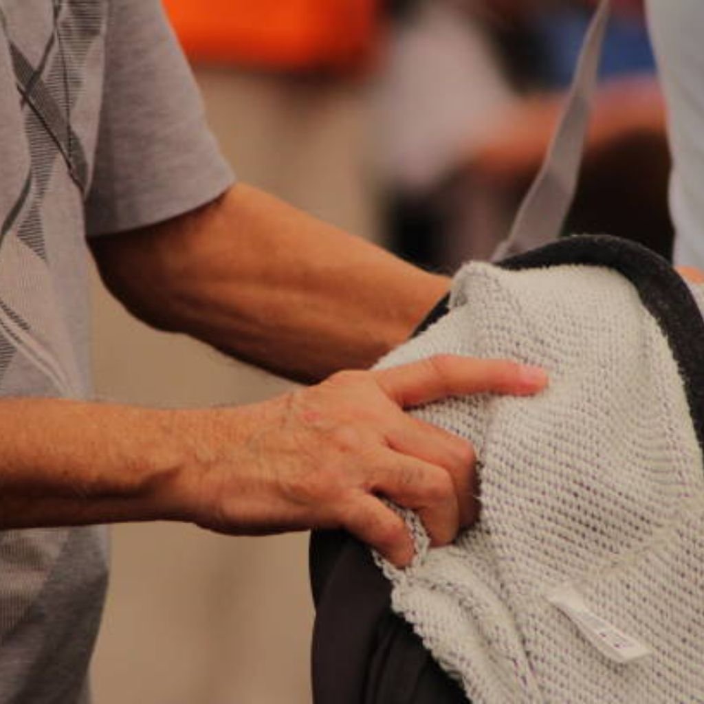 "Close-up of a man's arm and hand resting on a white military-inspired winter jacket with black trim, worn over a gray patterned shirt"
Sweat Shield Performance Knit:

