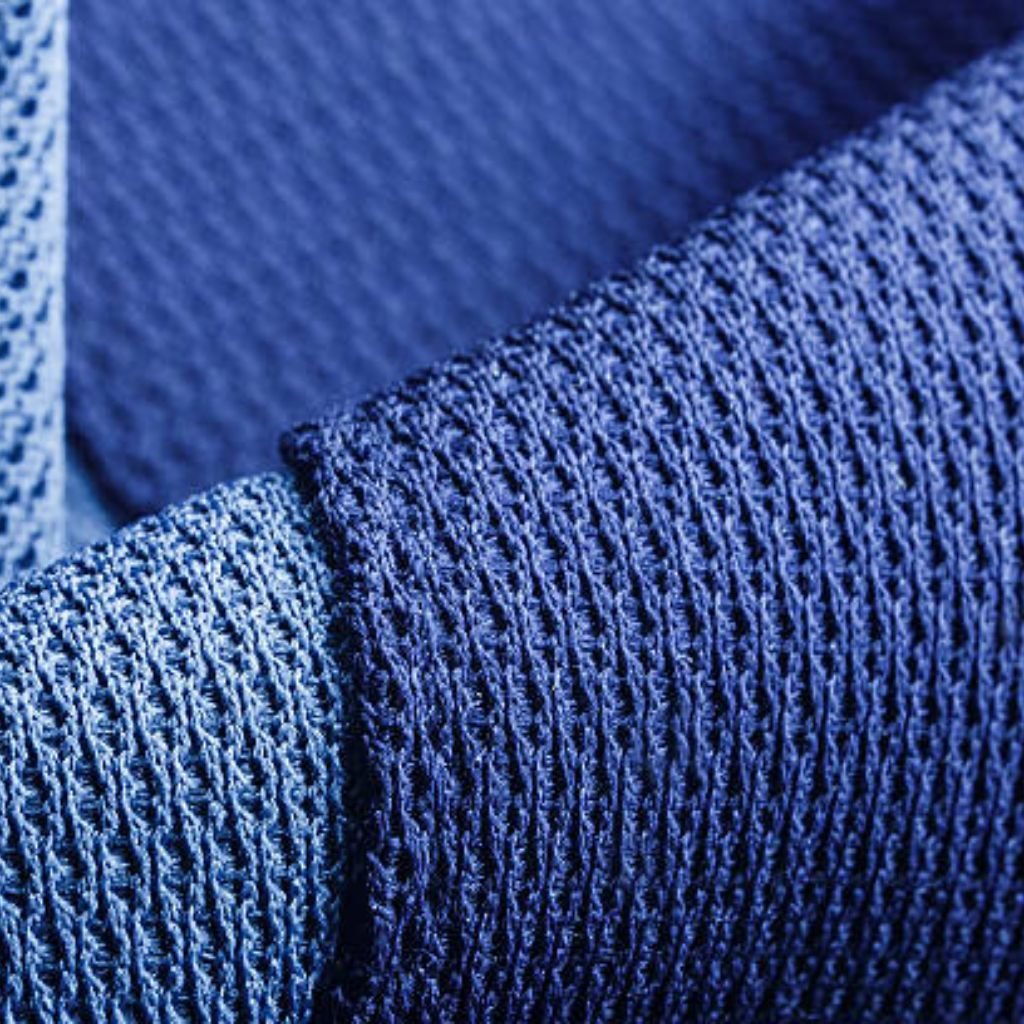 "Close-up macro shot showing side-by-side textures of dark blue and light blue knitted fabric — visible interwoven fibers, subtle loop structure, and tiny knit holes; high-contrast lighting emphasizes tactile depth."

Dynamic Flex Sports Knit: