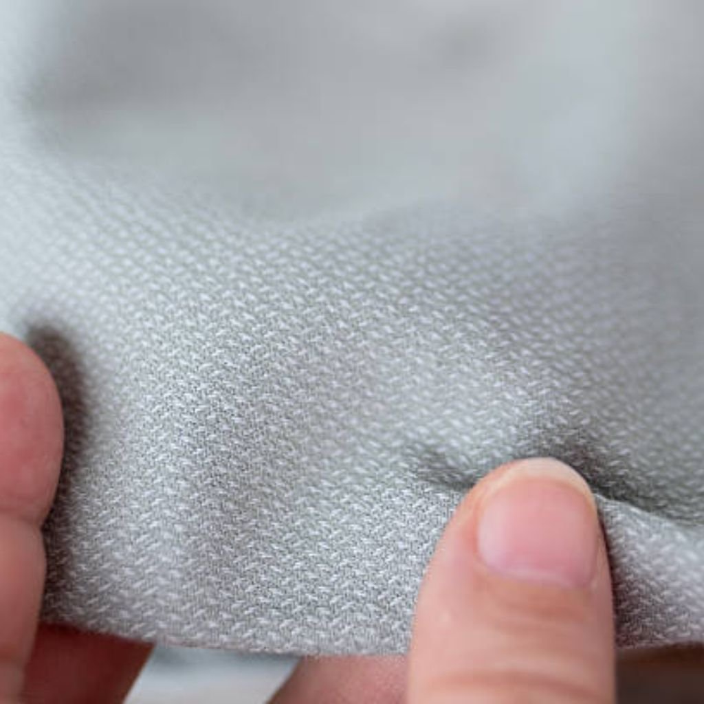 Neo Dry Tech Fabric: Ultimate Moisture Control for Athletes 11 Close-up of a hand touching a textured gray fabric with a subtle woven geometric pattern; soft lighting highlights surface detail and gentle indentation where finger contacts material.
Neo Dry Tech Fabric: