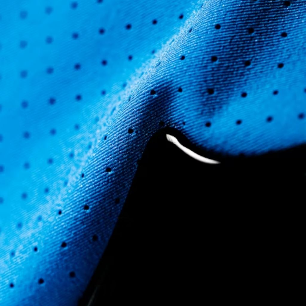 Close-up of blue breathable fabric with tiny perforations and a visible water droplet resting on the surface.Infinity Cool Tech Knit: