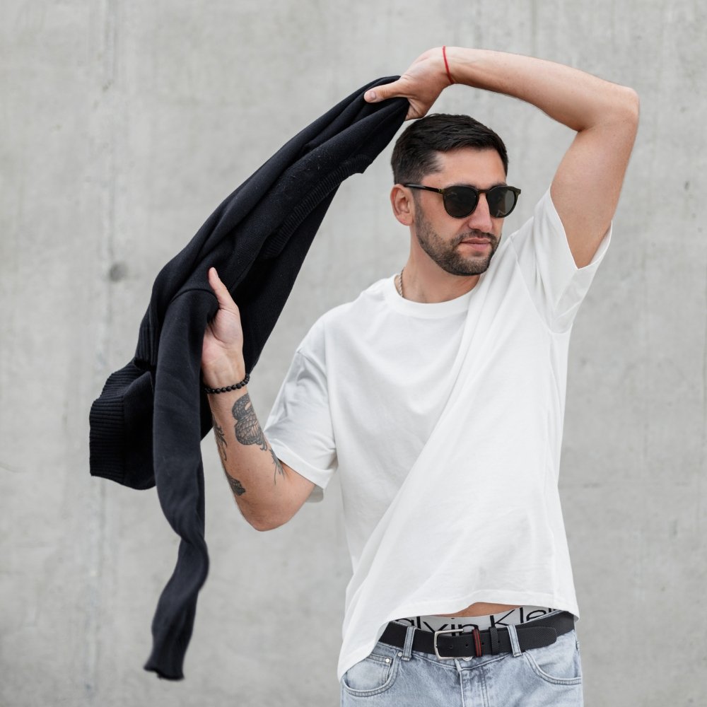 Muscle Fit T-Shirts That Define Your Body Shape 8 Man wearing a style muscle-fit T-shirt with sunglasses and holding a black hoodie over his shoulder outdoors.