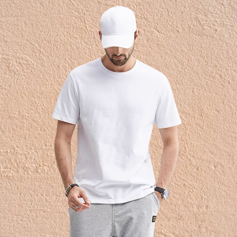 Portrait of a man wearing a plain white crew-neck T-shirt, standing outdoors against a textured beige wall background.