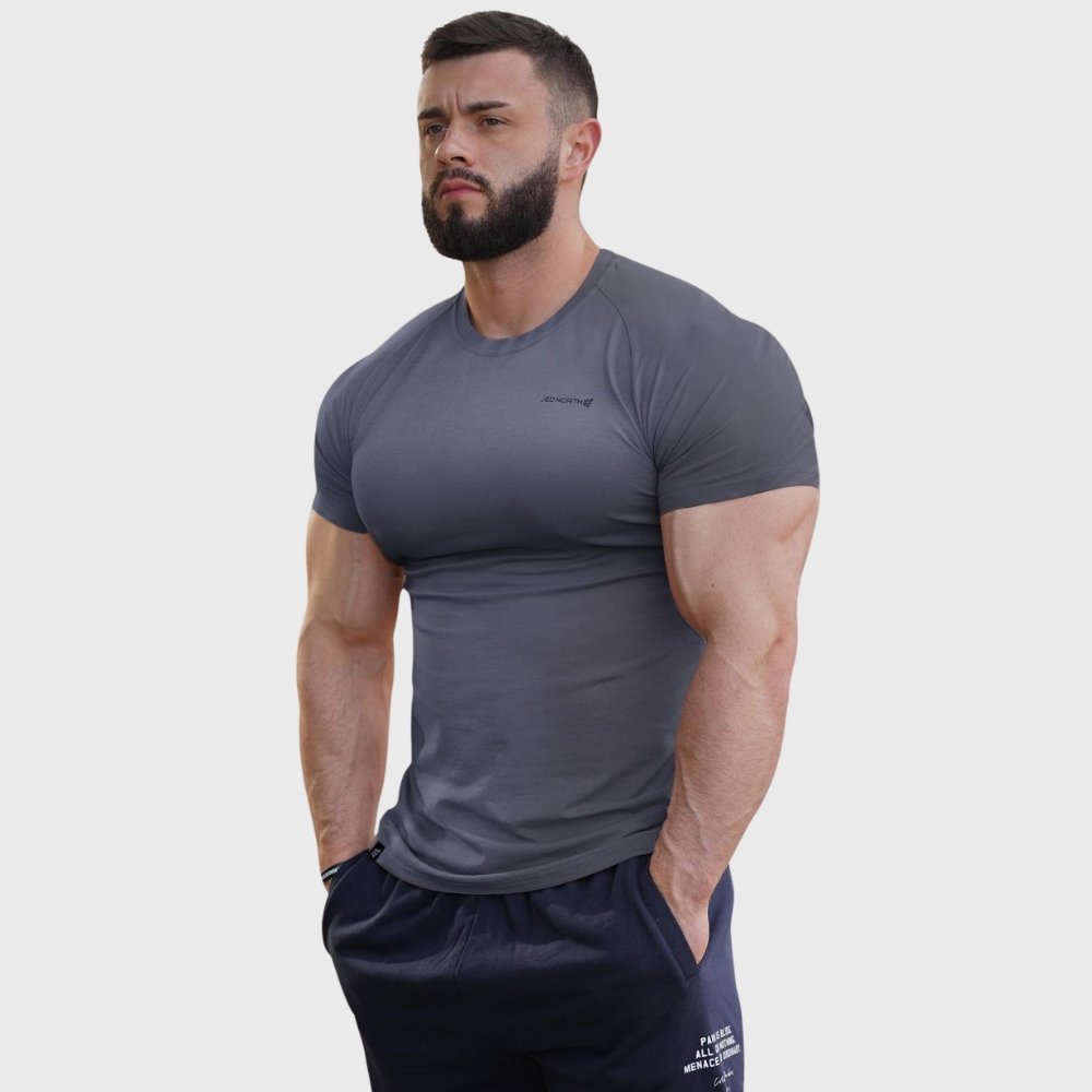 Muscle Fit T-Shirts That Define Your Body Shape 7 Muscle-fit dark gray T-shirt on a model, short sleeves with a small chest logo, paired with navy jogger-style pants.