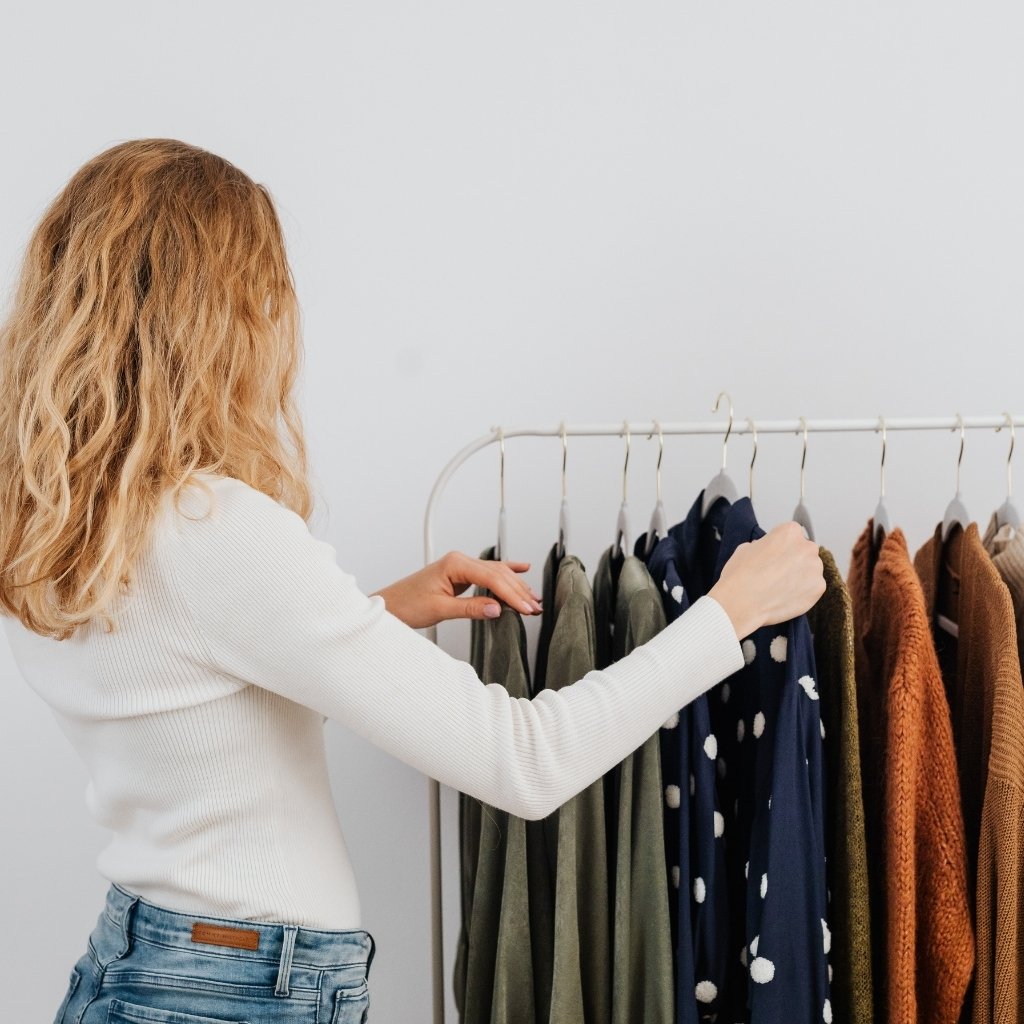 Woman browsing and holding a t-shirt on a clothing rack with neatly organized tops in a minimalist room.