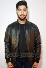 A young man in a black leather jacket and black shirt standing against a white background, holding a relaxed pose.