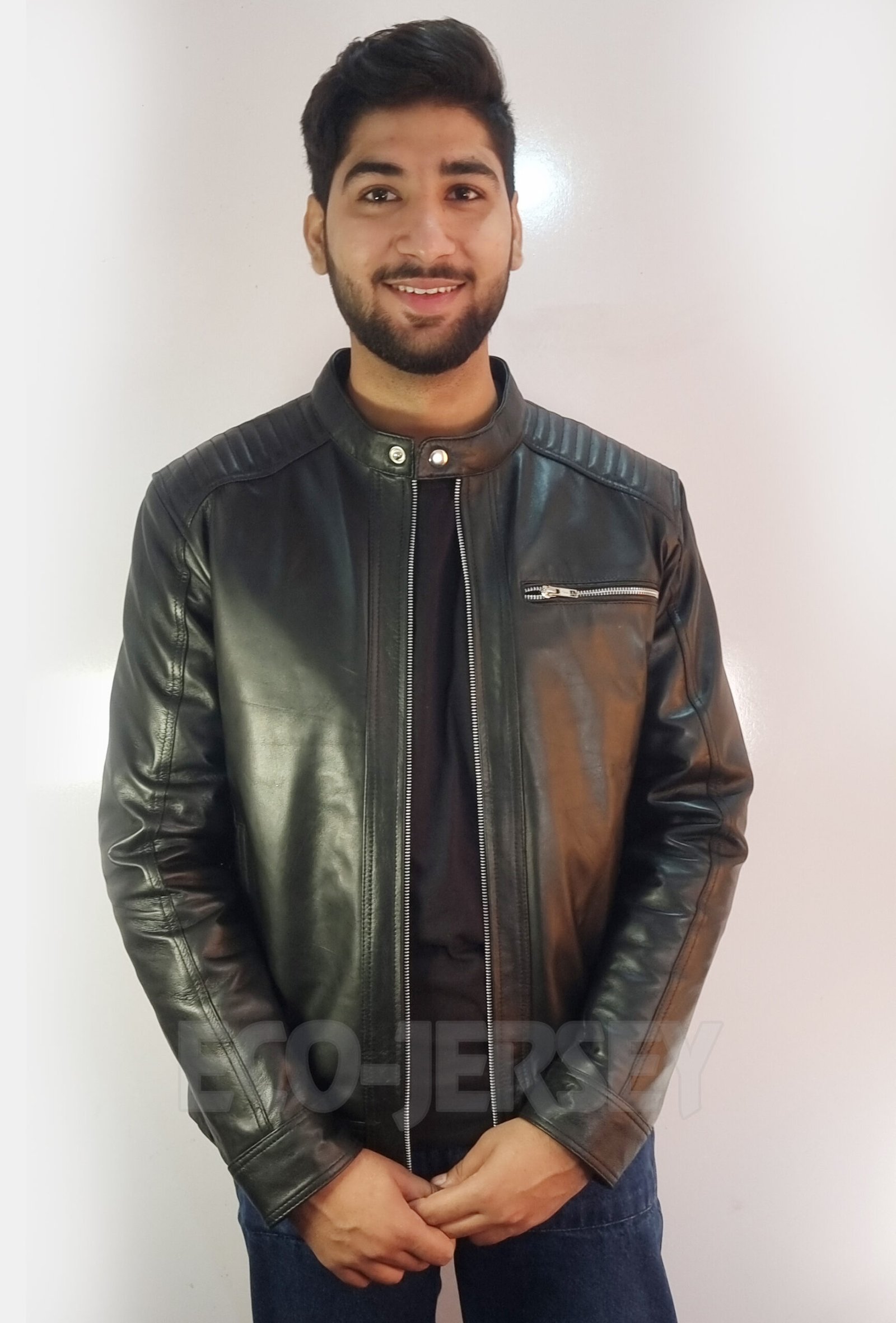 A male model wearing a black leather jacket with a quilted shoulder design, standing confidently facing forward.