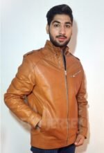 A young man in a brown full grain leather jacket with a zippered chest pocket and quilted shoulders poses as against a white background. Making a uniqe pose by putting his hand in the side pock of the leather jacket.