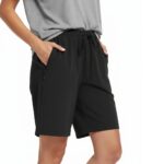 Woman wearing black golf shorts with a drawstring waist, front pockets, and a gray top, standing against a white background.