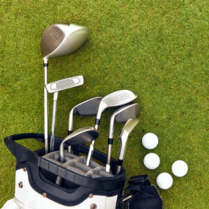 A golf bag on the grass containing several golf clubs with white golf balls nearby
