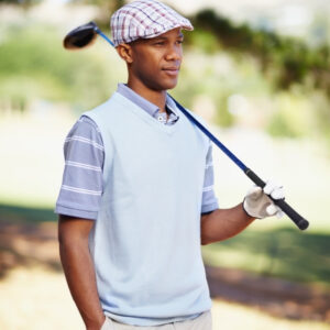 A golfer wearing a light blue polo over a gray striped short-sleeve shirt, holding a golf club on a sunny golf course.