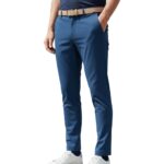 Man wearing blue slim-fit stretch golf pant with tan belt and white sneakers, posing with one hand in pocket against a white background