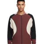 Man wearing a burgundy, cream, and black color-blocked bomber jacket with a zip front and light brown collar, photographed in a studio.