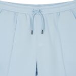 Close-up of light blue athletic shorts showing an elastic waistband with a drawstring and metal tips, textured fabric, vertical front seams, and a left side pocket.