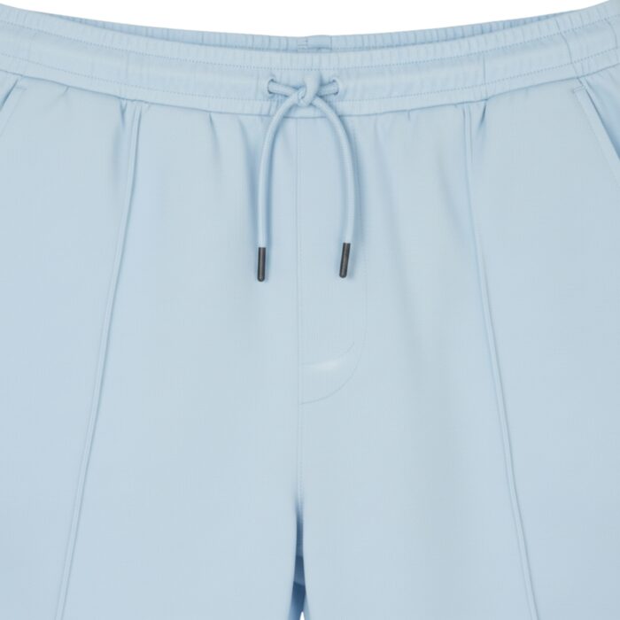 Close-up of light blue athletic shorts showing an elastic waistband with a drawstring and metal tips, textured fabric, vertical front seams, and a left side pocket.