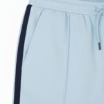 Close-up of light blue athletic shorts showing a dark blue side stripe, a drawstring at the waistband, and a side pocket.