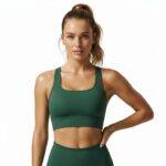 Woman standing against a white background wearing a matching green sports bra and leggings, with her hair in a ponytail and one hand on her hip.