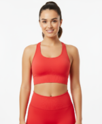 Smiling woman wearing a red racerback sports bra and matching high-waisted leggings, standing against a white background with her hair in a ponytail.