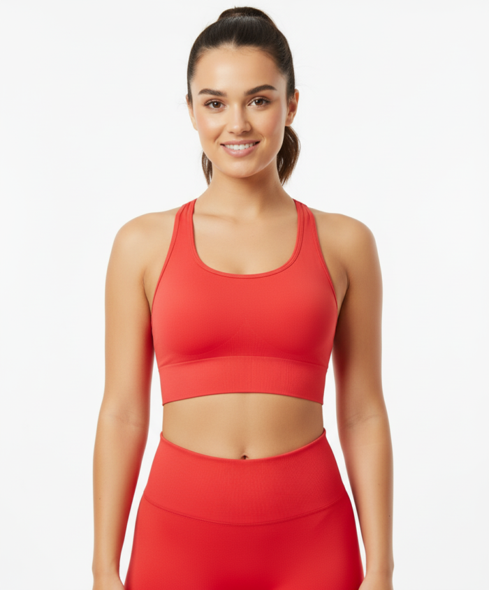 Smiling woman wearing a red racerback sports bra and matching high-waisted leggings, standing against a white background with her hair in a ponytail.