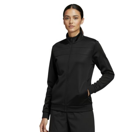 A woman stands against a white background wearing a black Adidas tracksuit with a zip-up jacket featuring a stand-up collar and matching shorts. She has one hand in the jacket pocket.