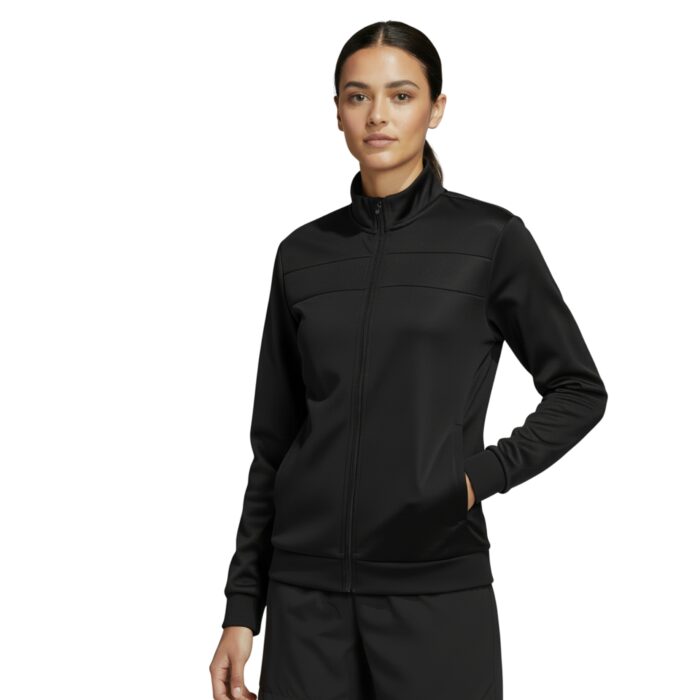 A woman stands against a white background wearing a black Adidas tracksuit with a zip-up jacket featuring a stand-up collar and matching shorts. She has one hand in the jacket pocket.