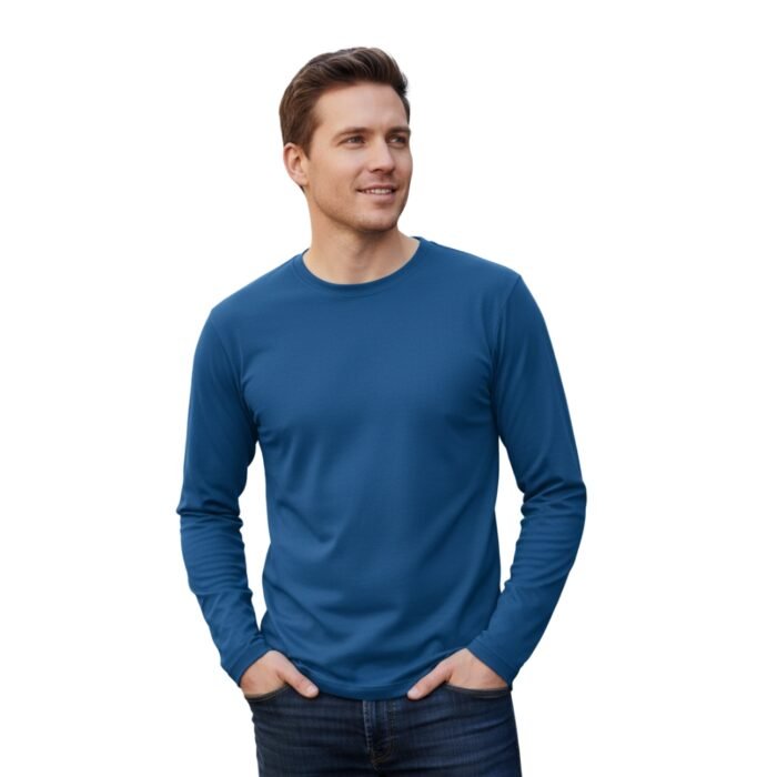 A person wearing a relaxed-fit, long-sleeve crew-neck blue shirt stands casually with hands in pockets, smiling softly to the side; neutral background suggests everyday authenticity.