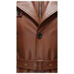 Close-up view of a brown leather trench coat highlighting the lapel, buttons, zipper, and belt detail.
