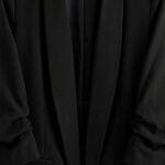 Close-up of black blazer fabric showing the weave, stitching, and seam detail.