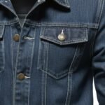 Men’s dark blue denim jacket material closeup showing gold button detailing and contrast topstitching