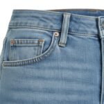 Close-up view of light-wash denim fabric showing the front pocket, rivet, and topstitching details on women's capri pants.