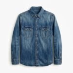 Front view of a light blue men's denim shirt with button-down collar, full button placket, and two chest pockets laid flat on white.