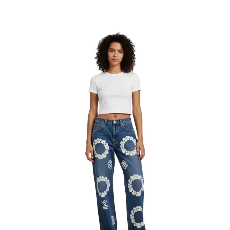 Woman wearing white crop top and blue distressed denim jeans with white floral embroidery and decorative patterns, posing against a plain white background.