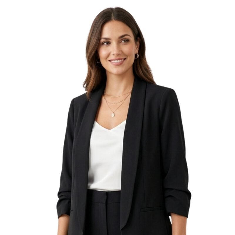 Woman wearing a black blazer over a light top and trousers, standing front facing against a plain background.