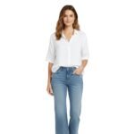 A woman in a white short-sleeve shirt and light-wash denim capri pants, standing and smiling against a white background.