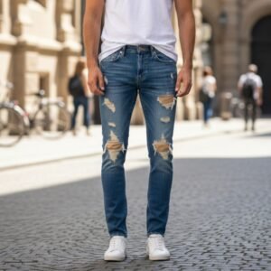 Model wearing ripped blue jeans, white t-shirt, and white sneakers on a cobblestone street.