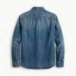 Back view of a folded light blue men's denim shirt with pointed collar and buttoned cuffs on a white background.