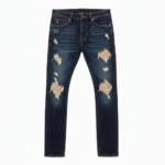 Dark wash blue jeans on white background with heavy distressing and large rips throughout the legs.