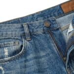 Closeup of blue denim baggy short with distressed pocket and button detail