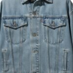 Light-wash denim jacket detail view showing a button-front placket, flap chest pockets with button closures, and button cuffs.