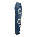 Womens blue distressed denim jeans with white floral embroidery and tribal-inspired side panels, shown flat against a white background.