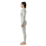 Side view of a woman wearing a light grey seamless ski base layer set with long-sleeve top and leggings, standing against a white background.