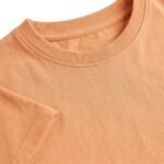 Close-up view of the peach crew neck t‑shirt fabric, showing texture and stitching details.