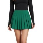 Woman wearing a green golf skort and matching top, shown from the front. Skort has a smooth pull-on waistband, above-the-knee length, and small logo icon on the hem