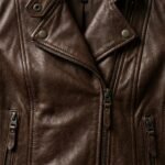 Close‑up of a women’s brown leather biker jacket showing front zipper and lapel details.