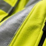Close-up of custom yellow hi-vis softshell jacket showing silver reflective strip stitching and zipper detail – quality workwear