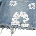 Close-up of distressed denim shorts fabric showing ripped threads, frayed edges, and stitch detailing.