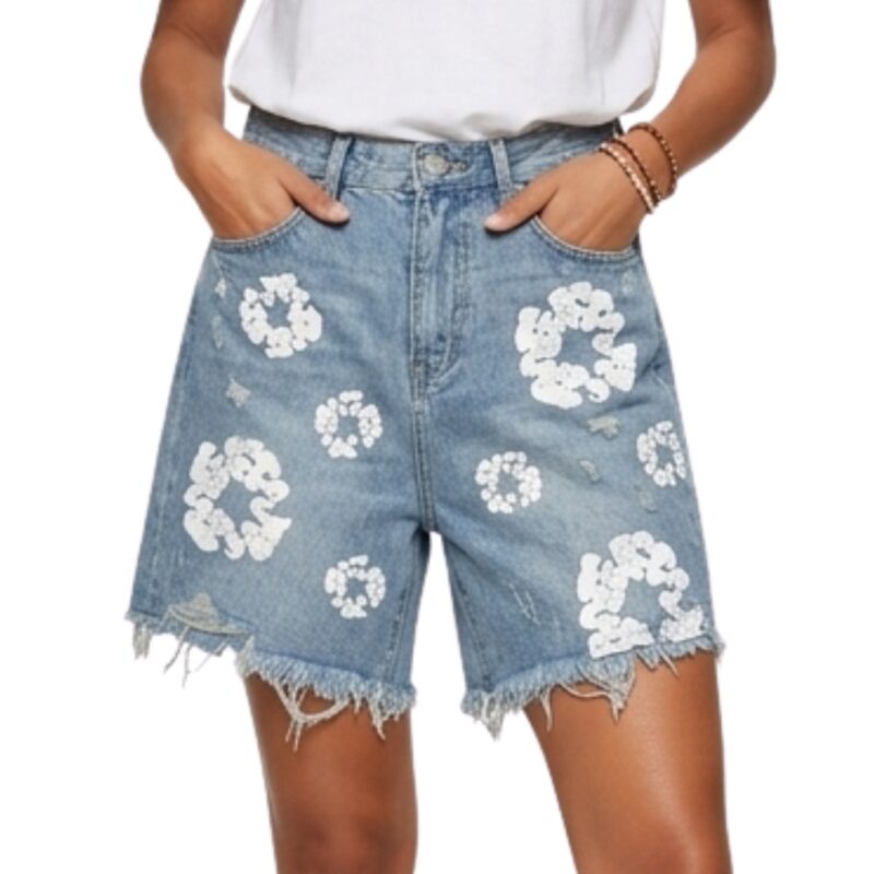 Female model wearing distressed denim shorts and a white crop top, standing in a relaxed pose.