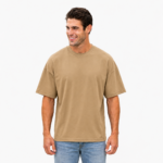 Smiling male model wearing a custom khaki beige drop shoulder oversized t-shirt by Eco Jersey, paired with light blue jeans, showcasing the relaxed oversized fit and dropped shoulder seam